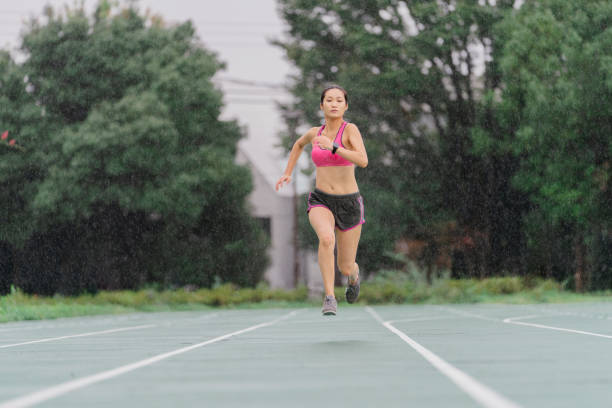 Young female sprinter running in rain A young female sprinter is running in rain. all weather running track stock pictures, royalty-free photos & images
