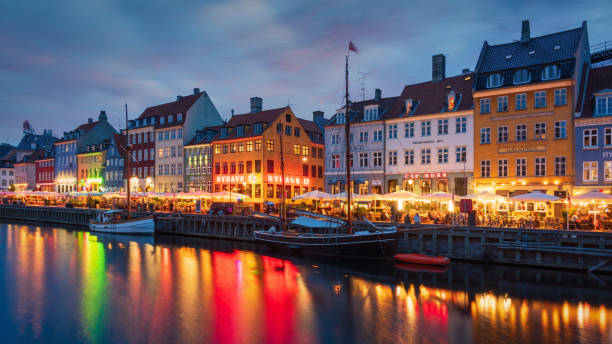 Copenhagen Nyhavn Nightlife Twilight Denmark Nightlife in the famous illuminated Nyhaven District of Copenhagen in sunset twilight. Crowds of People walking along the channel to visit Restaurants and Bars in colorful traditional danish houses. Unrecognizable Crowd of People, several cityscape logo signs not in focus. Nyhavn, Copenhagen, Denmark, Nordic Countries, Europe nyhavn stock pictures, royalty-free photos & images