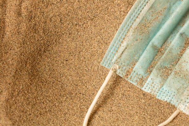istock Waste during COVID-19. Scrapped to ocean coronavirus single-use face masks. Environmental and coastal plastic pollution. Trash on the beach that threatens the health of the oceans. 1276986625