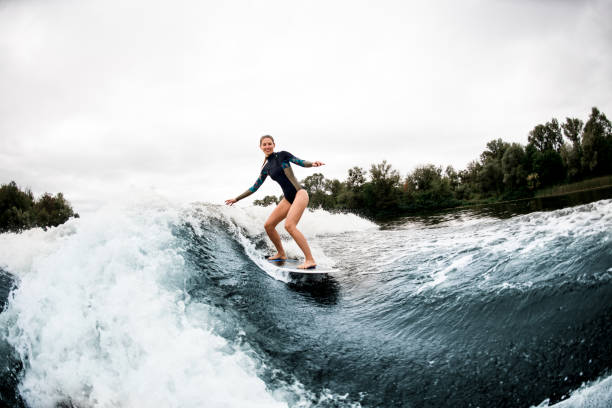 istock Cheerful woman in wetsuit rides down on surf style wakeboard on wave 1276991659