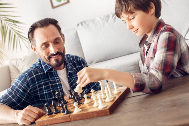 istock Father and little son at home sitting at table playing chess dad looking ceerful at boy holding knight thoughtful 1276995833