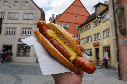 Giant German sausage with mustard in a bun, held up high on a street corner