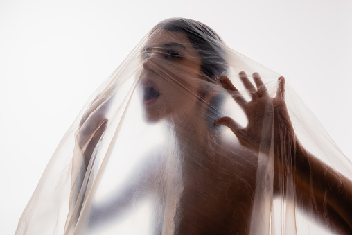 trapped brunette woman screaming through polyethylene isolated on white, ecology concept
