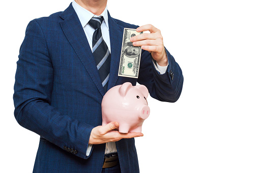 Businessman putting one hundred dollar into piggy bank. Businessman in suit is holding piggy bank. Finance Savings concept