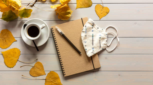 istock Workspace with notebook, mask, pen, autumn leaves, and coffee cup. 1277004717