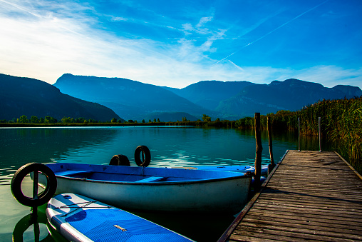 small blue and white early morning boat moored at the Caldaro lake pier in Bolzano, Italy