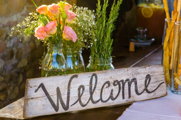 signo de bienvenida pintado en madera junto a flores rosas - warm welcome fotografías e imágenes de stock