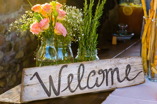 Welcome sign painted on wood next to pink flowers