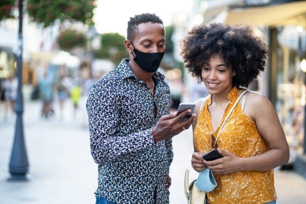 istock Afro Couple wearing protective face mask walking on the streets and using smart phone, during COVID-19 1277010569