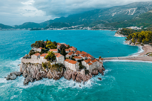 Luxury resort of Sveti Stefan seen from above in the emerald waters of the Adriatic sea and with Budva and mountains in the background.