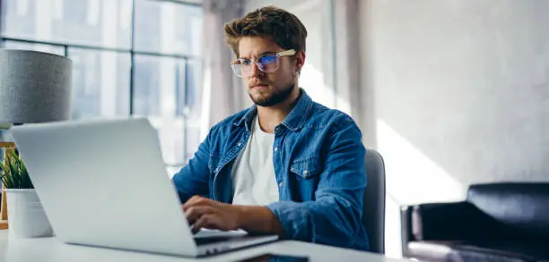 Photo of Man typing on laptop. Modern businessman at sunny office. Freelancer at work. Blogger or journalist writing new article