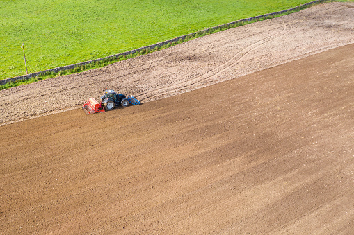 The view from a drone of a tractor pulling a seed drill which is sowing wheat to be harvested next year.\nThe location is a rural area of Dumfries and Galloway in south west Scotland.