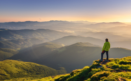 Hombre deportivo en el pico de la montaña mirando en el valle de la montaña con rayos de sol en la puesta de sol de colores en otoño en Europa. Paisaje con viajero, colinas de niebla, bosque en otoño, cielo increíble y luz del sol en otoño photo