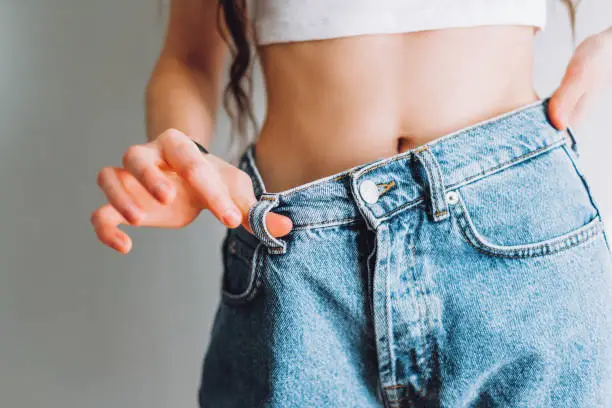 Slimming concept. Young woman holds jeans in her hand, shows a thin waist Slim female body in large jeans. Successful weight loss. High quality photo