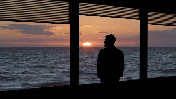Photo of The lonely man standing near the window on the beautiful seascape background