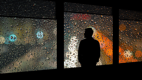 The lonely man standing near the window on the rainy background