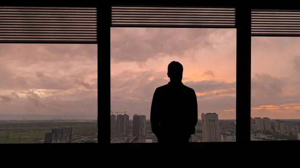 Photo of The lonely man standing near the window on the urban background