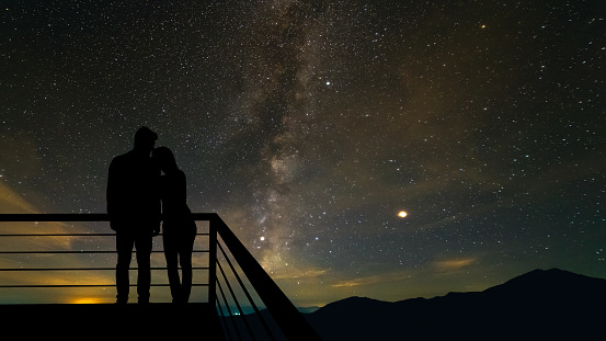 The romantic couple standing on the balcony on the scenic starry sky background