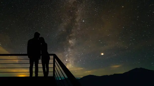 Photo of The romantic couple standing on the balcony on the scenic starry sky background