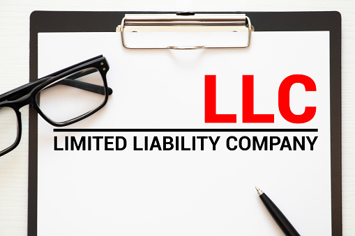 LLC Limited Liability Company - handwriting on paper with cup of coffee and pen, acronym business concept.