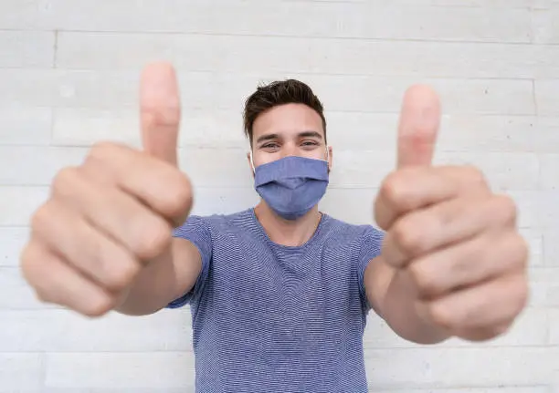Photo of Young man with protective face mask shows thumbs up - Positive attitude to the current epidemic situation and measures - Focus on his face