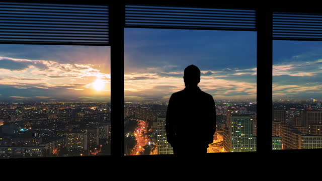 The man stands near the window on the night urban background. time lapse