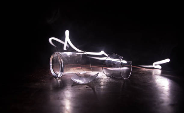 istock Broken glasses on wooden table at dark toned background with fog. Selective focus 1277029219