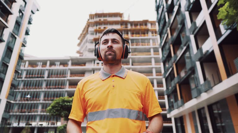 Builder covers his ears, ear muff to protect workers ears. Construction worker wearing protective ear defenders. Concept of construction, taking care of safety during work. Protection against injury