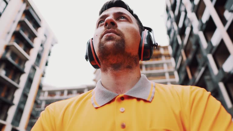 Builder covers his ears, ear muff to protect workers ears. Construction worker wearing protective ear defenders. Concept of construction, taking care of safety during work. Protection against injury