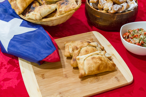 September 18th, Chilean food Independence Day Concept, Fiestas patrias. Chilean typical menu on independence day party, September 18th. Beef rustic empanadas, Pebre (Tomatoes sauce with white onions), Pastel de Choclo (Corn Pie), Calzones Rotos (Dessert) and tipical play trompo and a Chilean Flag around the table.