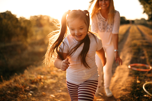 Kid with Downs syndrome and her mother running in meadow