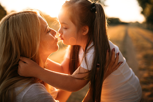 Kid with Downs syndrome and her mother bonding outdoors in warm summer day