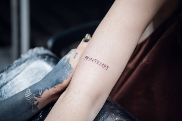 The hand of a tattoo artist a girl with tattoos and a newly made tattoo in the form of a word on the hand of a freckled client stock photo