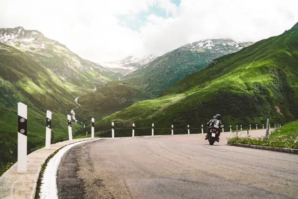 Lonely motorbiker driving on Furka pass road in the mountains.