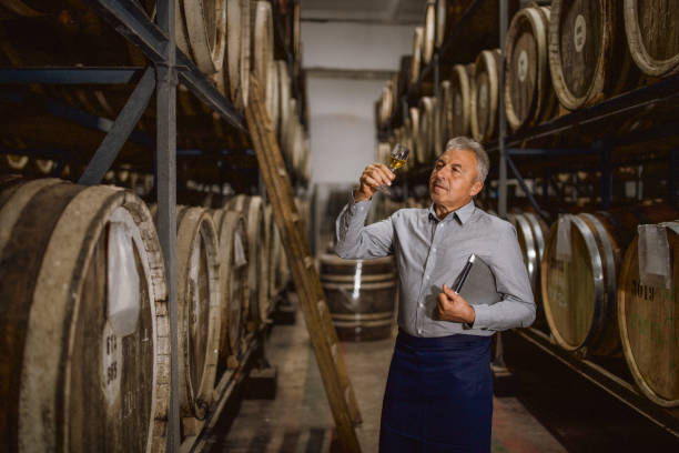 distillery manager nimmt proben aus den fässern und probiert den whiskey - schnapsbrennerei stock-fotos und bilder