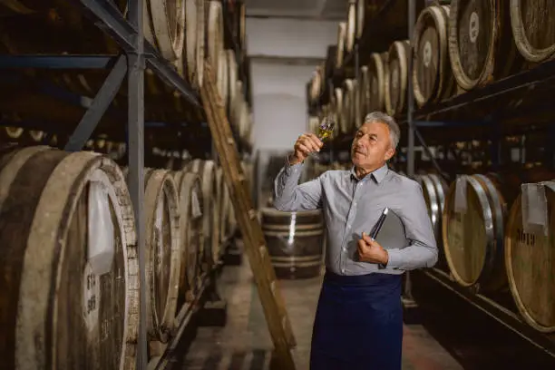 Distillery senior male manager is taking samples from the barrels and trying the whiskey