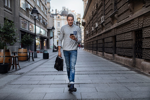 Portrait shot of a young man walking down a city street while using a mobile phone