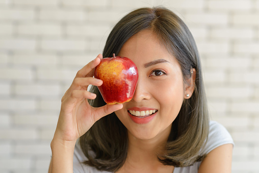 Portrait of smiling beautiful young asian woman holding red apple. close up
