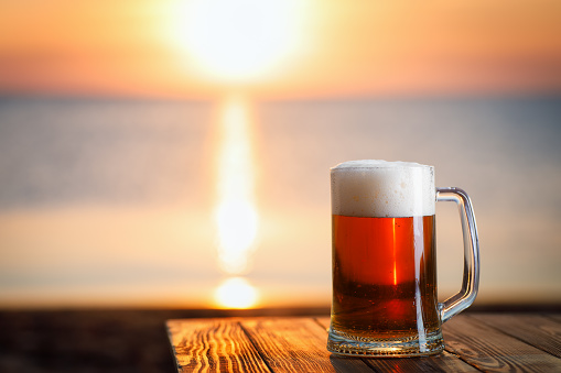 mug of beer with froth at the edge of table with sea on the background