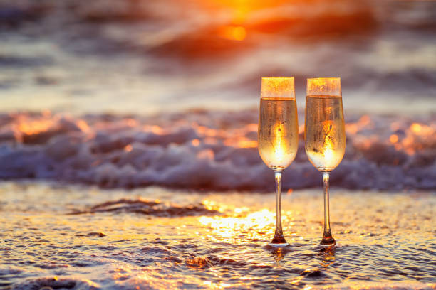 two glasses of champagne on the beach at sunset with sea on the background