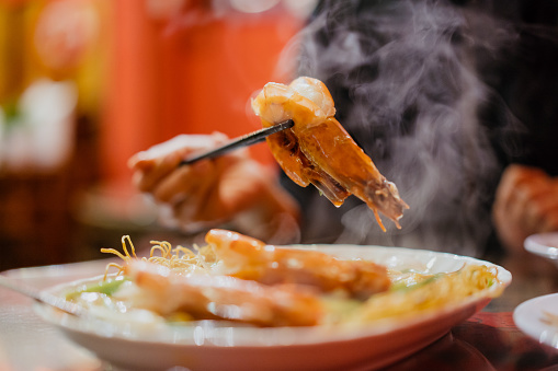 Young woman eating fresh prawn yee mee in plate with chopsticks