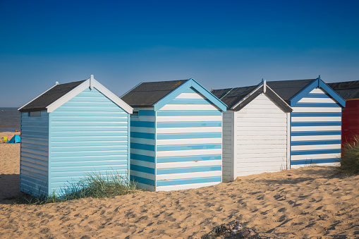 A row of colourful beach huts under a blue sky at Southwold beach in England