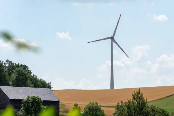 Wind turbine in open fields in farmland supplying green or renewable energy and electricity from natural resources against a cloudy blue sky