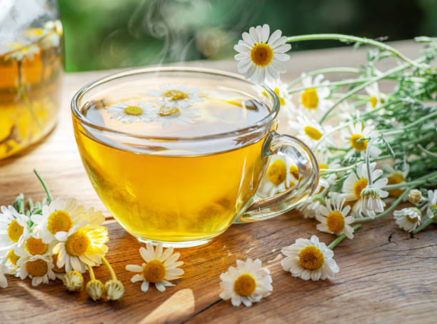 camomilla alle erbe e fiori di camomilla vicino alla teiera e bicchiere da tè su tavolo di legno. sfondo rurale. - chamomile foto e immagini stock