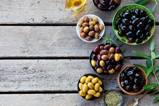 Assortment of fresh olives on a plate with olive tree brunches. Wooden background. Copy space. Top view.
