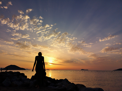 Silhouette of Young Woman with Long Skirt Standing on the Beach During Sunset at Aegean Sea