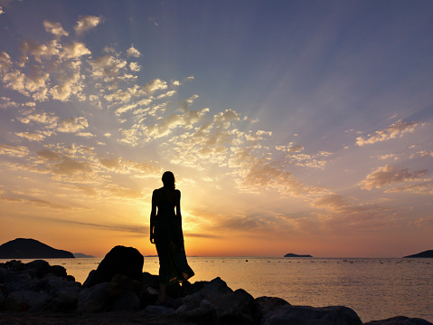 Silhouette of Young Woman with Long Skirt Standing on the Beach During Sunset at Aegean Sea