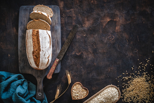 Wholegrain rye bread loaf with vintage knife and cereal grains assorted over dark wooden background