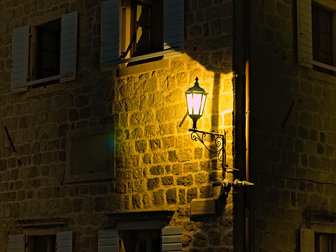 Perast, Montenegro  - October 27, 2019: illuminated street lamp on a stone house wall with surveillance cameras and street signs