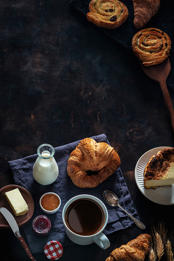 Coffee breakfast with pastries croissants, butter, cheesecake homemade on dark background